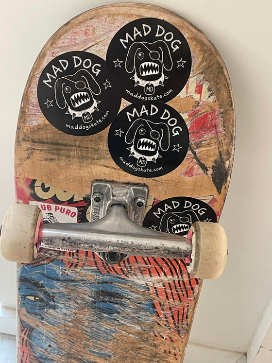 Underside of a skateboard covered in Mad Dog stickers